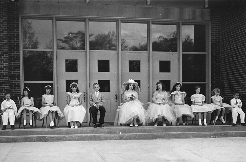 Black and white photograph of the May Day court. The students are posed in front of the original main entrance to Navy Elementary School. 