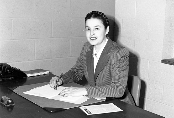 Black and white photograph of Principal Harrison seated at her desk. The walls are unadorned because the school had only recently been completed. 