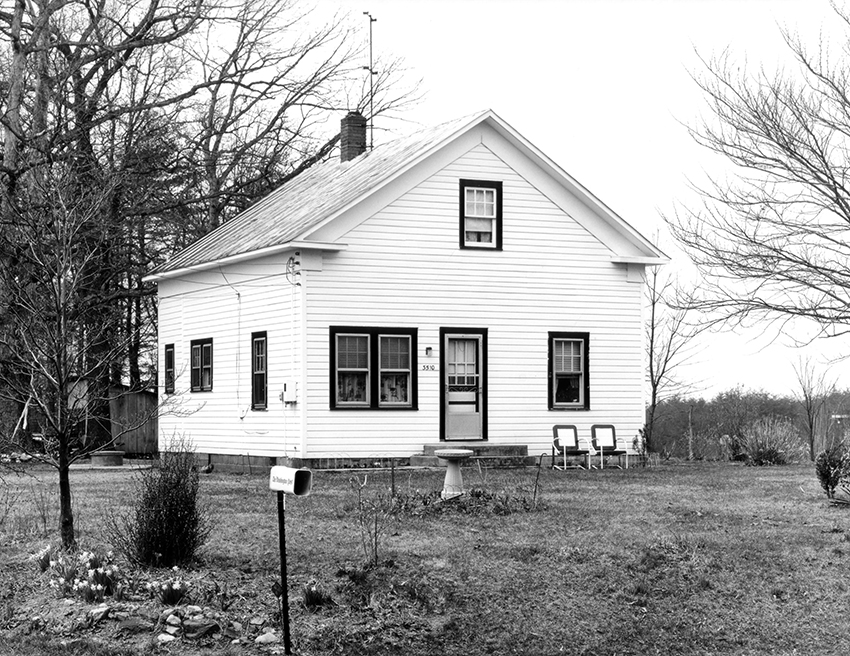 Black and white photograph of a small house with white siding.